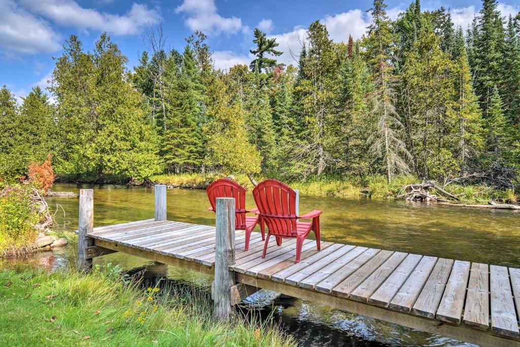twee rode stoelen op een steiger boven een rivier bij Riverfront Traverse City Cabin Fish, Kayak and Tube in Traverse City