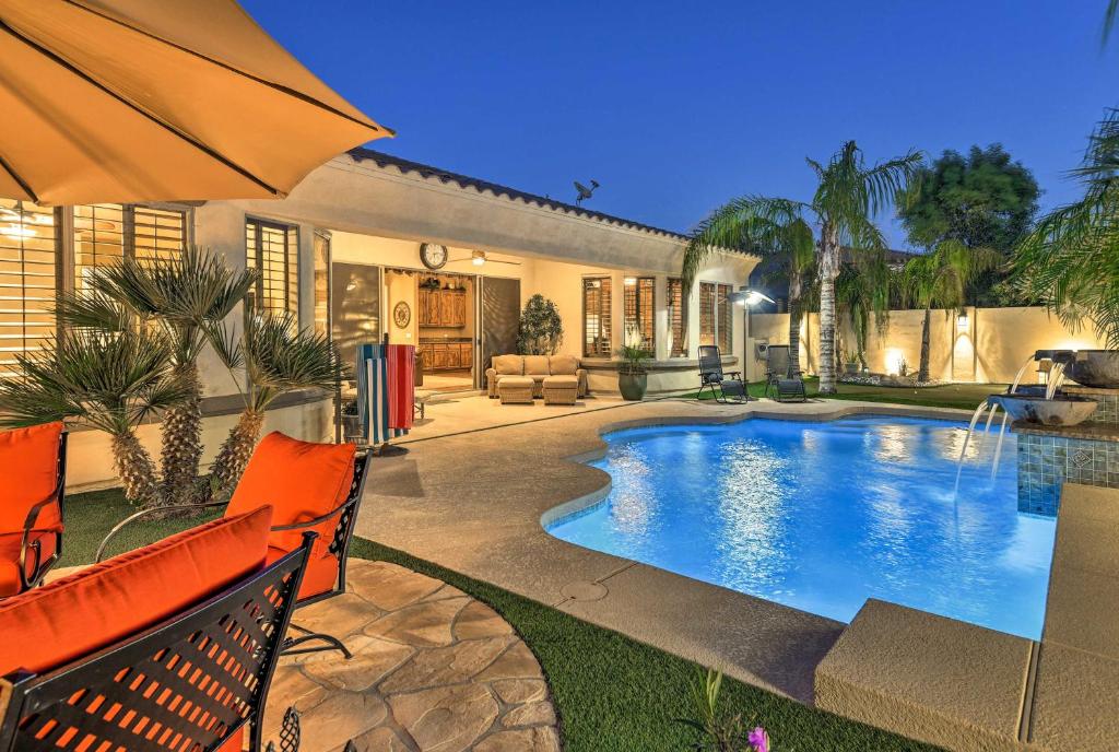 a home with a swimming pool and an umbrella at Luxe Gilbert Home with Heated Pool and Putting Green! in Gilbert
