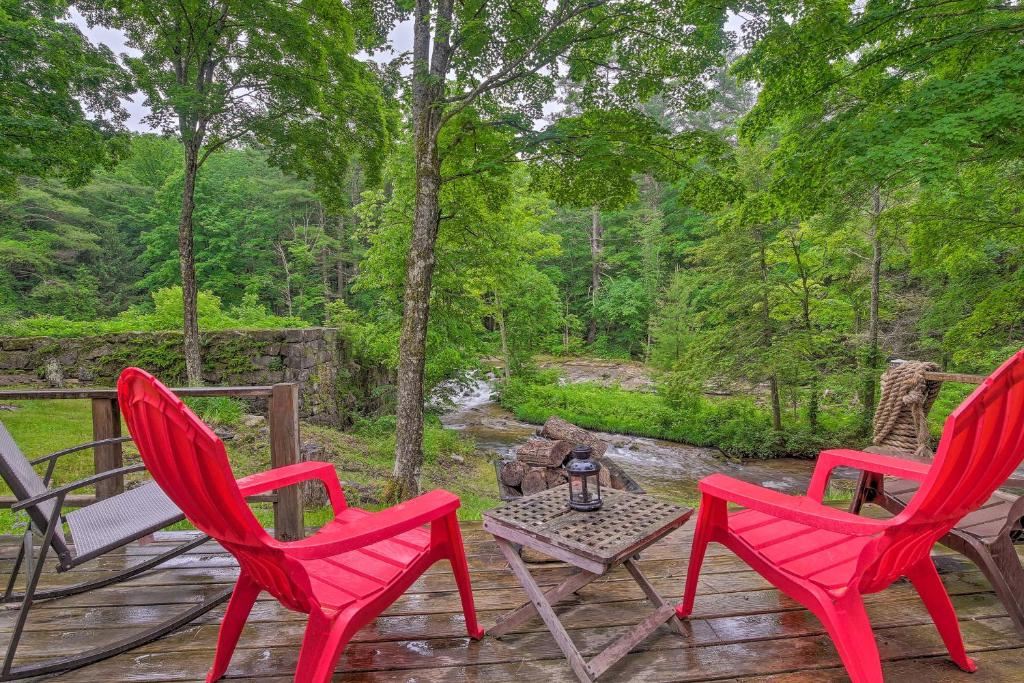 three red chairs and a table on a deck at The Mill River Cabin with Fireplace and River View! in Mill River