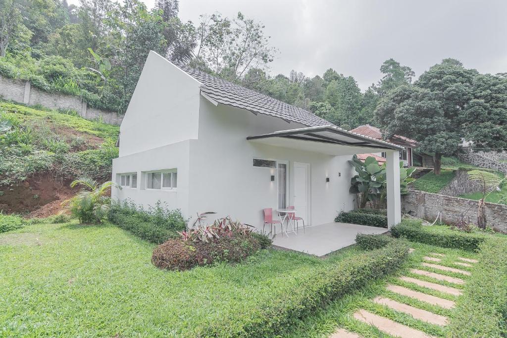 een wit huis met twee stoelen in een tuin bij RedDoorz Resort Syariah near D'Castello Ciater Subang in Subang