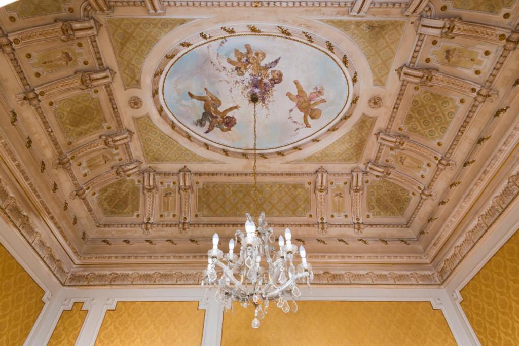 カターニアにあるPalazzo Arcidiacono - luxury holidaysの天井にシャンデリアと絵画が飾られている