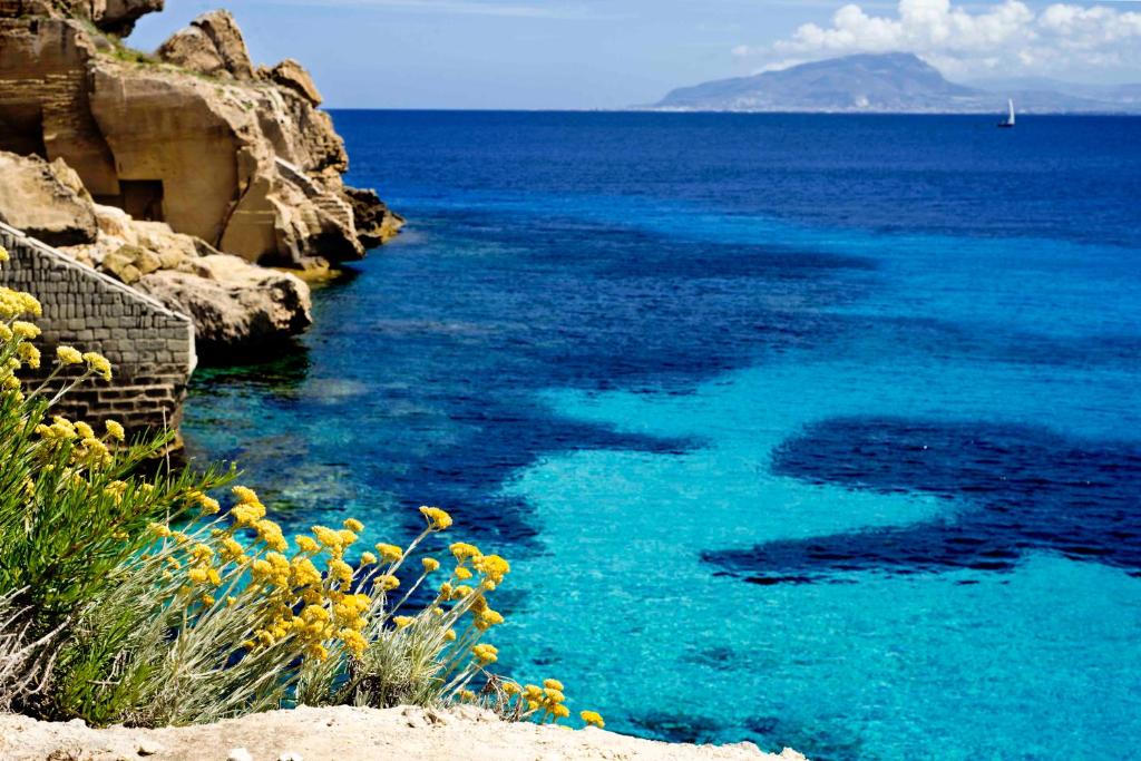 a blue body of water with yellow flowers in the foreground at Luxmarì Hotel & Spa in Castellammare del Golfo