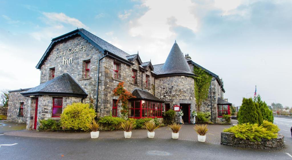 um grande edifício de pedra com janelas vermelhas num parque de estacionamento em The Yeats County Inn Hotel em Tobercurry