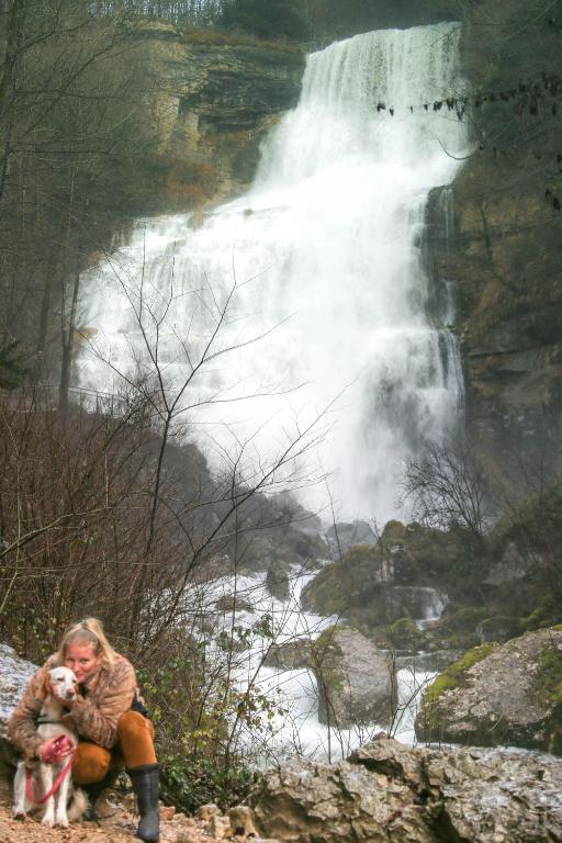 a woman holding a dog in front of a waterfall at le refuge des Marmottes in Saint-Laurent-du-Jura