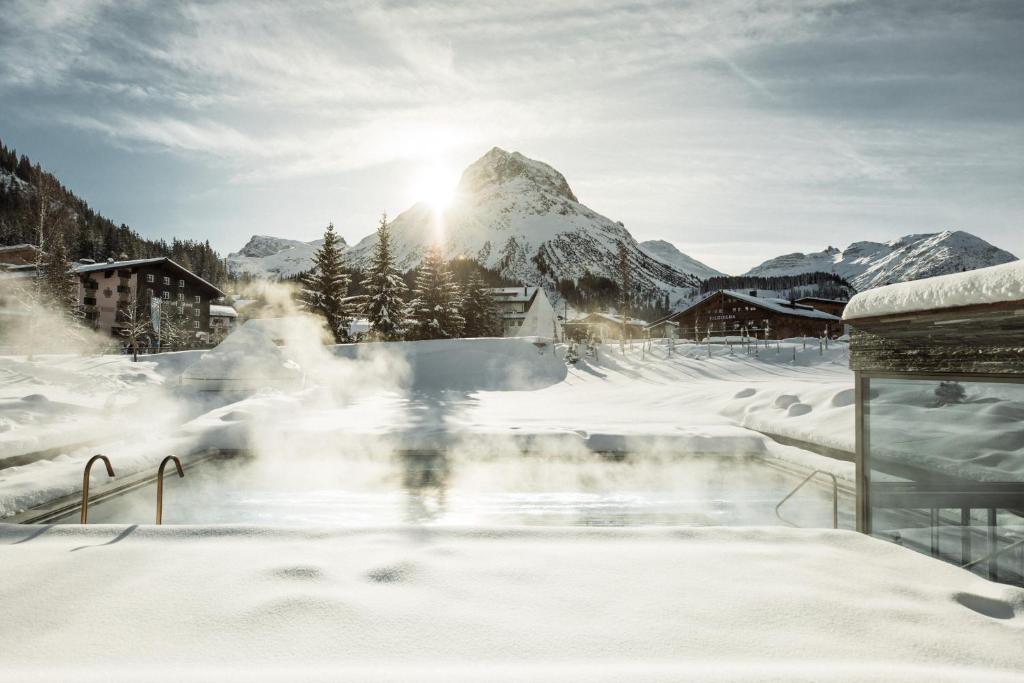 Beheizter Außenpool des Hotel Arlberg mit Schwimmern, umgeben von verschneiten Bäumen und Bergen, St. Anton
