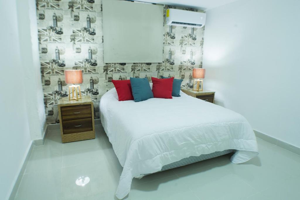 Un dormitorio con una cama blanca con almohadas rojas y azules en Malecon Rooms y Hotel, en Santo Domingo