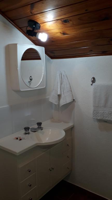 een badkamer met een witte wastafel en een spiegel bij Hospedagem Vó Rosa in Monte Verde