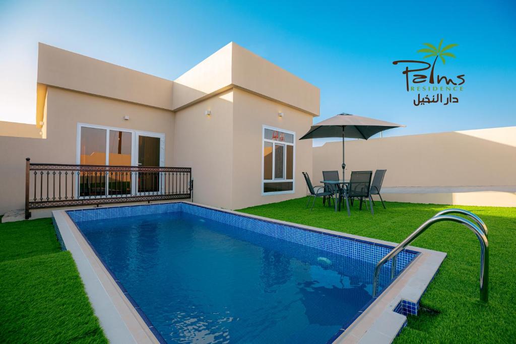 a swimming pool in front of a house with an umbrella at Palms Residence Inn دار النخيل in Nizwa