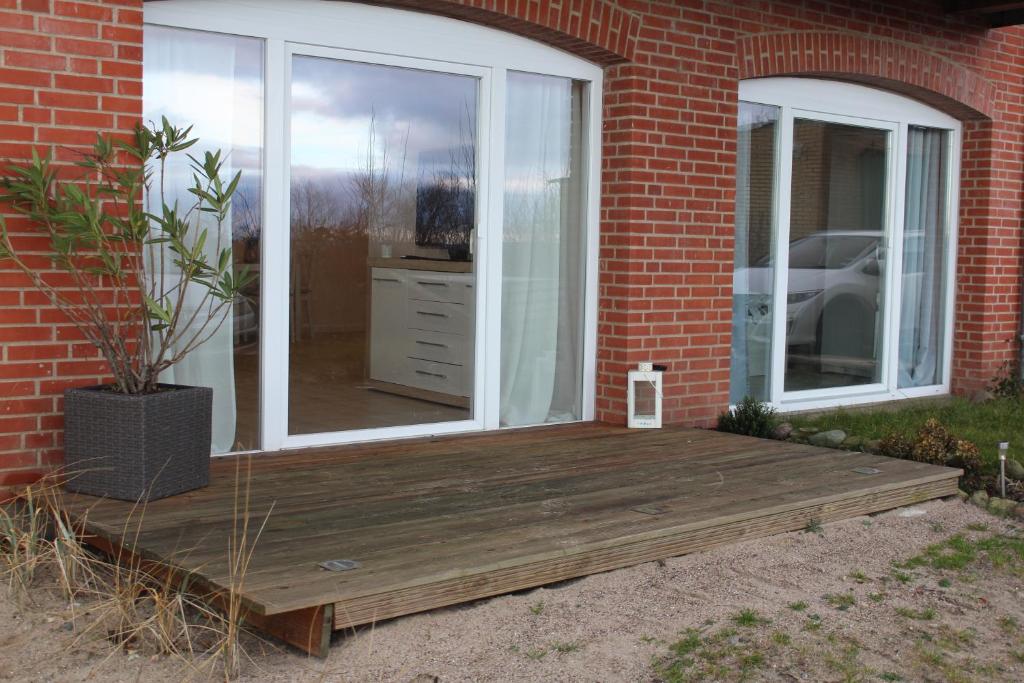 un porche con terraza de madera junto a un edificio de ladrillo en Augustenhof Ferien en Nordborg