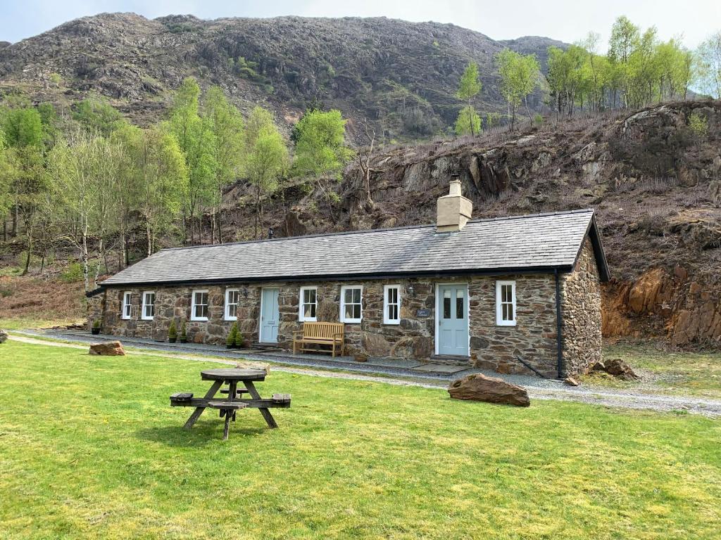 uma cabana de pedra com uma mesa de piquenique em frente em Sygun Cottage - Detached Cottage in the heart of the Snowdonia National Park em Beddgelert