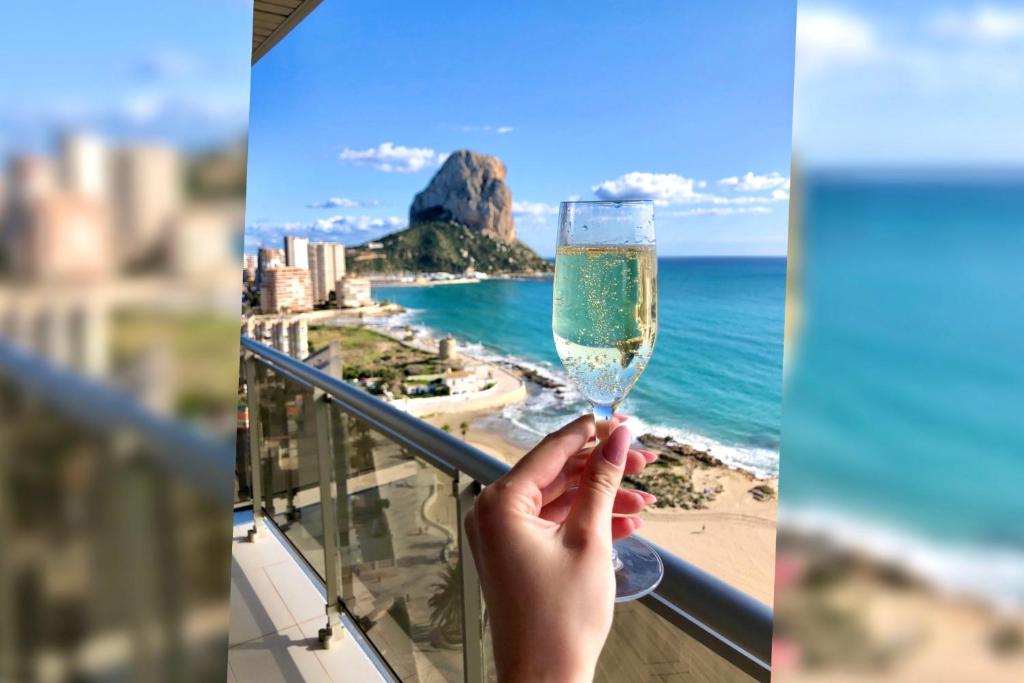 a person holding a glass of wine overlooking the beach at Vista Bella. Apartamentos in Calpe