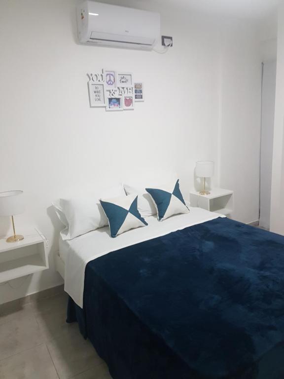 um quarto branco com uma cama com lençóis e almofadas azuis em Miguel Angel 5673 - A 5 minutos del Aeropuerto El Palomar em Villa Bosch