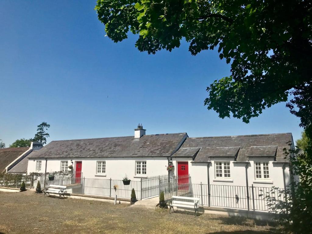 una casa blanca con puertas rojas y una valla en Kingsmills Cottages, en Artrea
