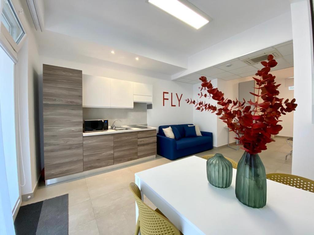 a kitchen and living room with a table with red flowers in a vase at BeeApartments in Bari