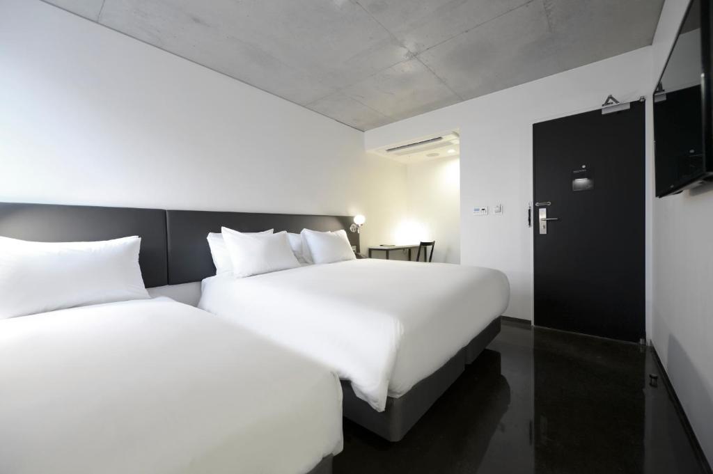 two beds in a hotel room with white sheets at Creto Hotel Myeongdong in Seoul