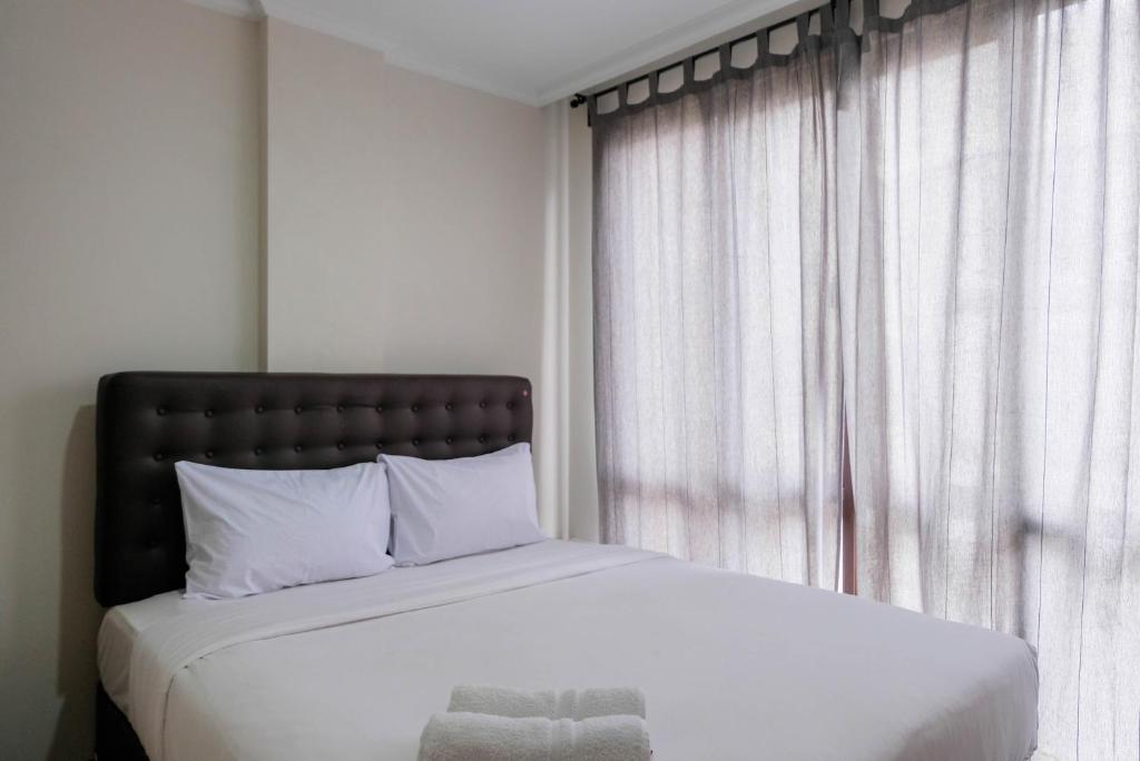 a bedroom with a bed with white sheets and a window at Convenient and Luxurious 2BR Asatti Apartment By Travelio in Pagedangan