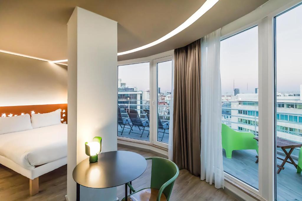A bedroom and sitting corner with a small round table, green chair and glazed balcony overlooking the city.