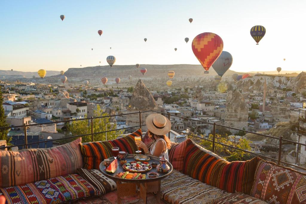 una mujer sentada en un sofá viendo globos de aire caliente en Mithra Cave Hotel, en Göreme