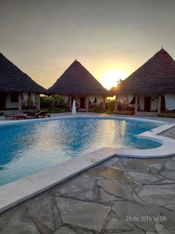 a resort swimming pool with huts in the background at Coral Village in Malindi