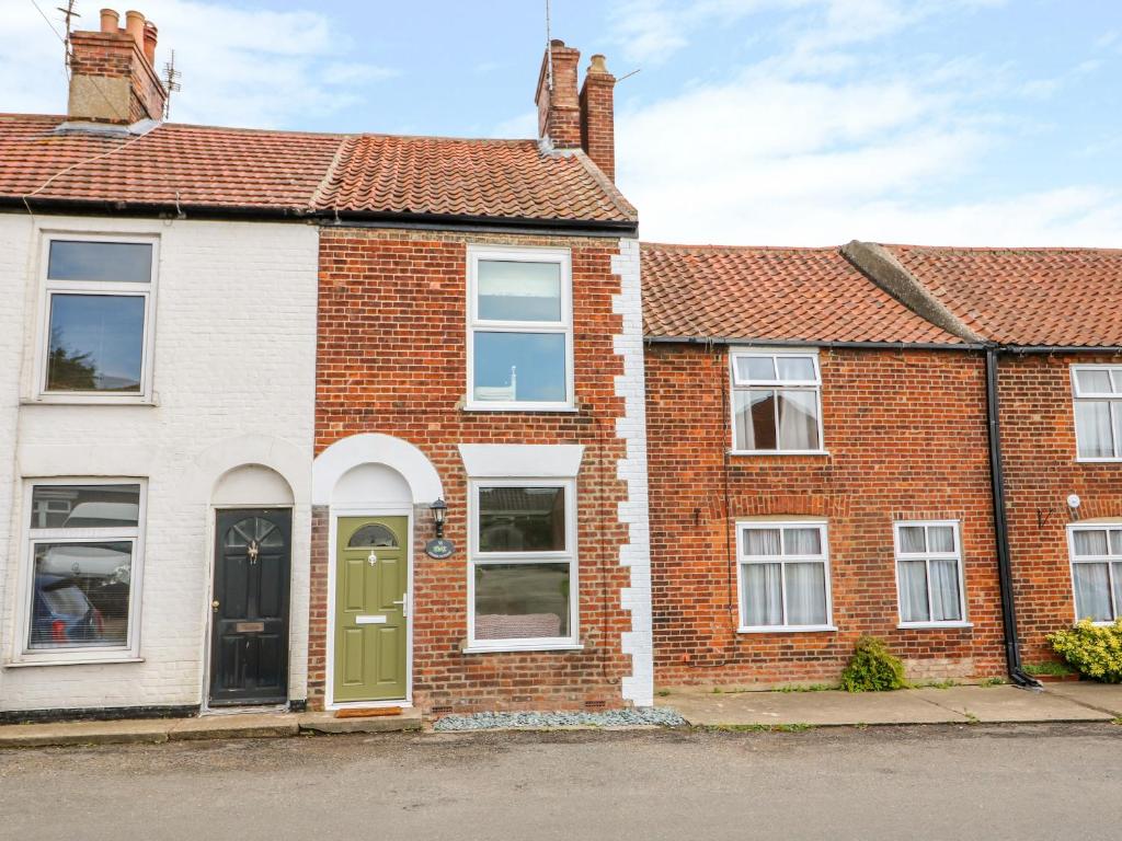 a brick house with a green door on a street at Coorie Cottage in Great Yarmouth