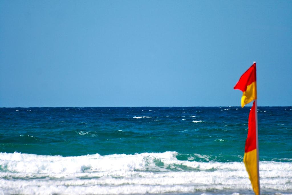 a red and yellow flag on the beach with the ocean at 29 @ One Lusty Glaze in Newquay