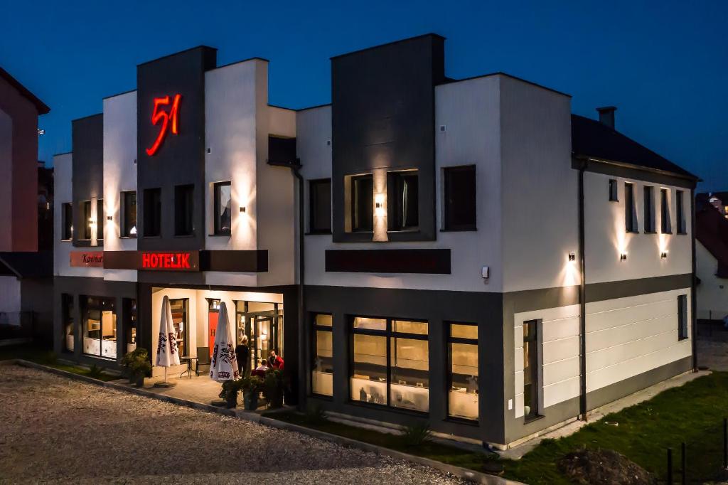 a large white building with a neon sign on it at Hotelik 51 in Pasłęk