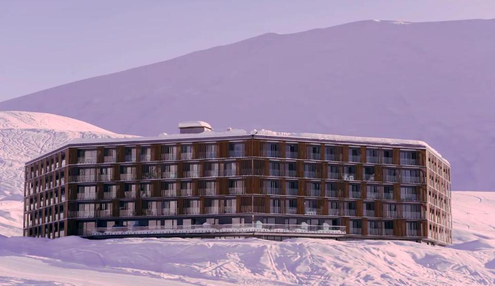 un edificio en la nieve con montañas en el fondo en Atrium New Gudauri by Gudauri Travel, en Gudauri
