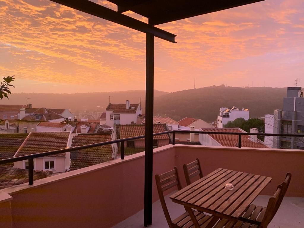 uma mesa de madeira e cadeiras numa varanda com um pôr-do-sol em Appartement3 avec terrasse et vue près d'Amoreiras em Lisboa