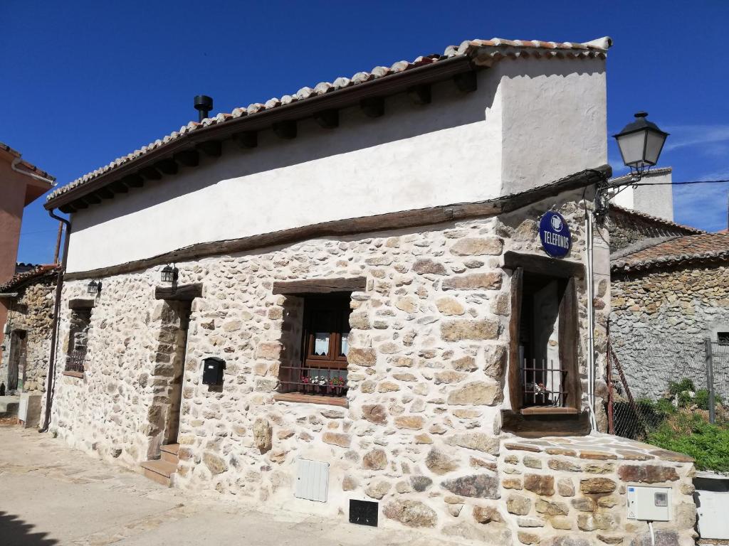 un antiguo edificio de piedra con dos ventanas y una calle en La Casita de Teléfonos, en Gargantilla del Lozoya