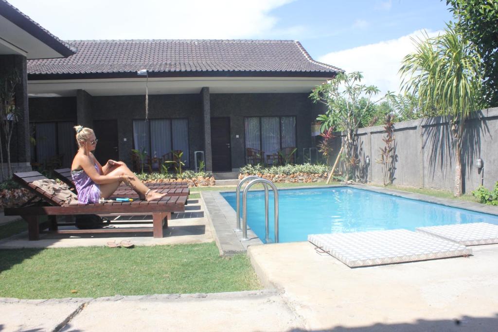 a woman sitting on a bench next to a swimming pool at Willy Homestay in Uluwatu