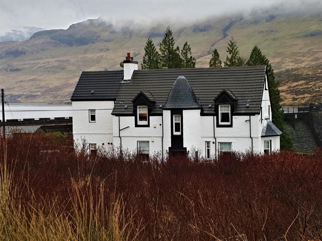 a white house with a black roof in front of a mountain at Loch Arklet House in Stirling