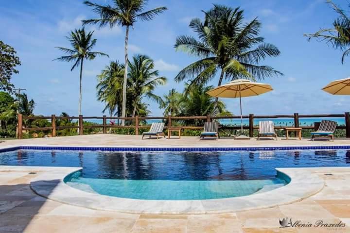 a pool with chairs and umbrellas and palm trees at Pousada Villa das Palmeiras in Paripueira