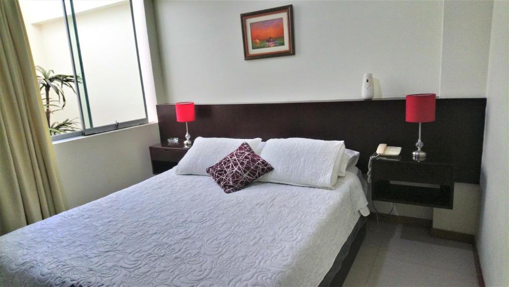 a bedroom with a white bed with two red lamps at Hotel Ivansino Inn in Chimbote