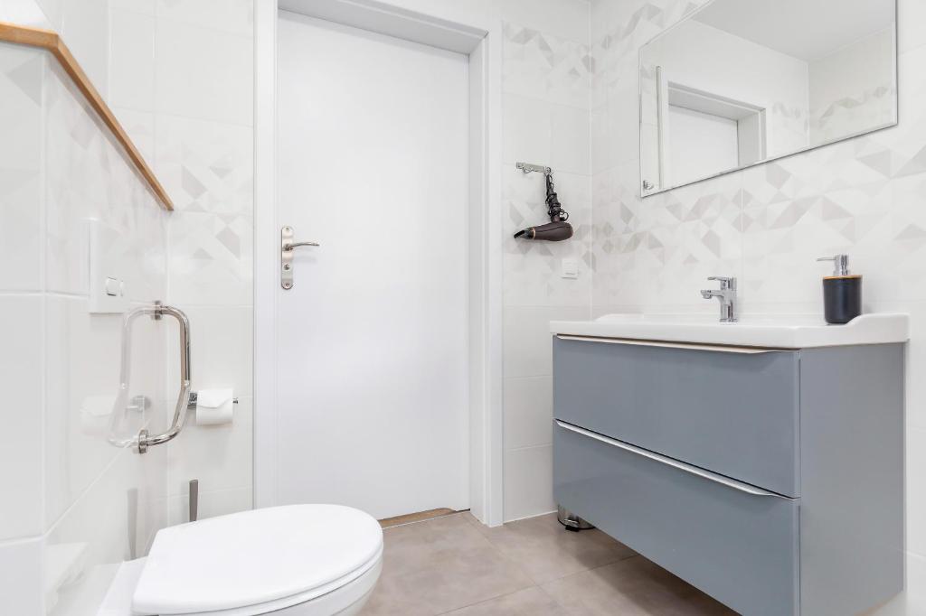 Clean white bathroom view showing toilet, sink vanity, wall mirror and hanging hairdryer.