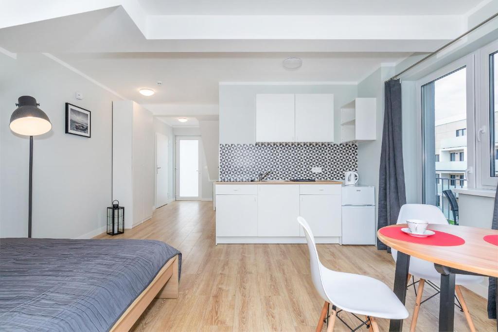 Studio interior with bed, round dining table, kitchenette, and large window letting in daylight.