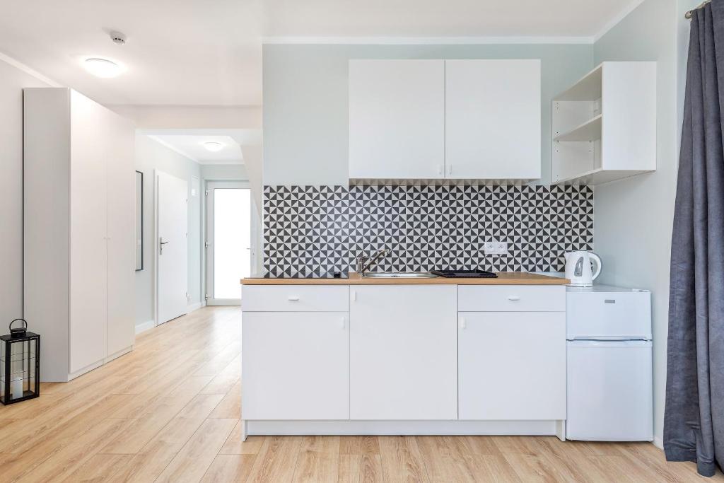 Compact white kitchenette with geometric tile backsplash, wooden countertop, mini fridge, bright hallway.
