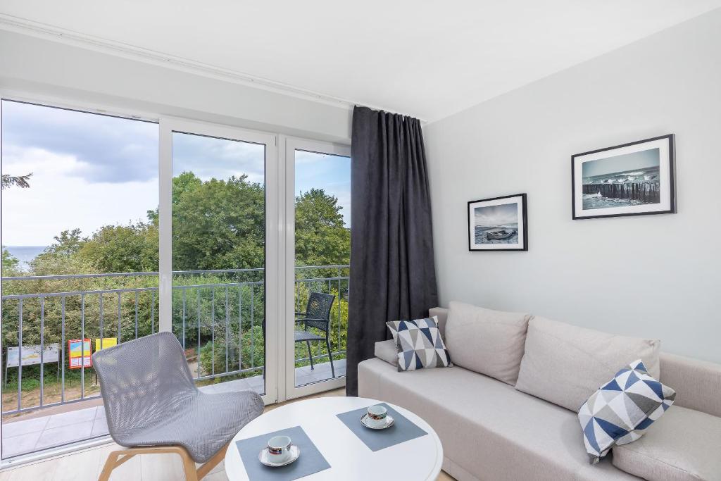 Bright living area with beige sofa, round coffee table with cups, chair, balcony overlooking green trees.