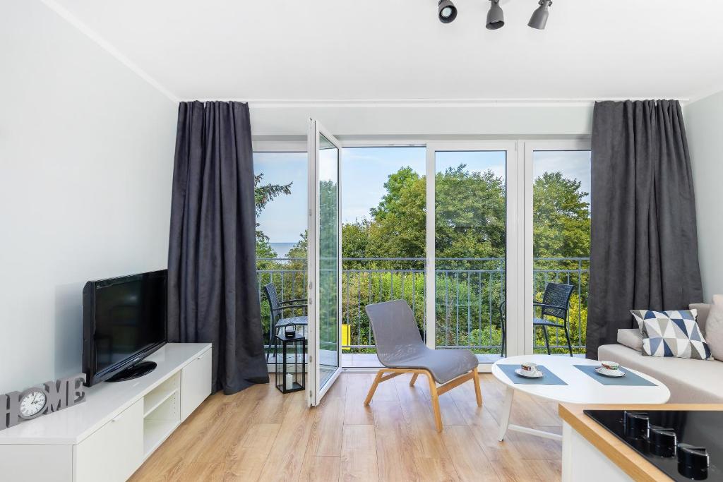 Open balcony doors revealing greenery, single lounge chair, TV stand and small balcony seating.