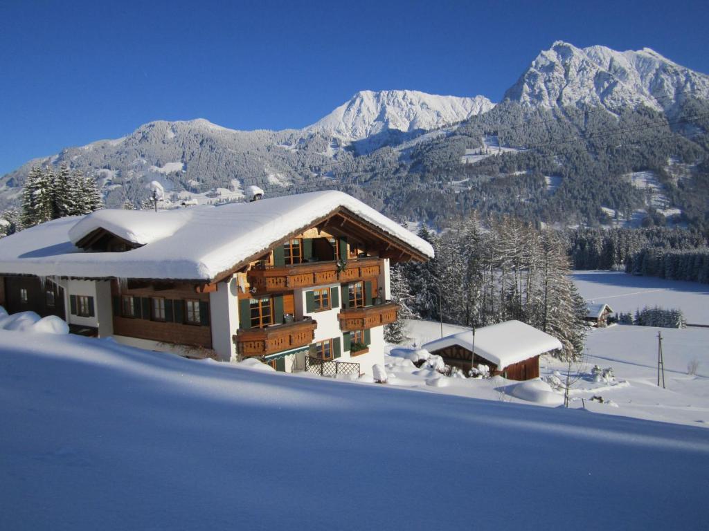 a house covered in snow with mountains in the background at Landhaus Eggensberger in Fischen