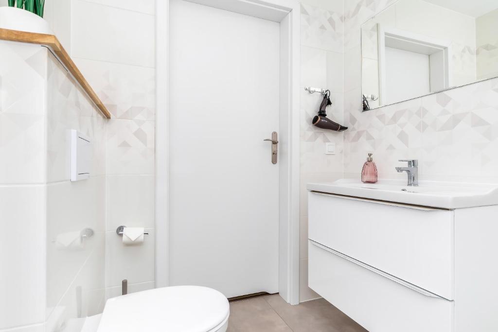 Small bright bathroom with white sink, mirror, wall-mounted hairdryer, and toilet, minimalist clean mood