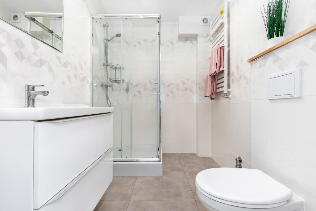 Clean white bathroom featuring glass shower enclosure, vanity sink, toilet, heated towel rack with pink towels.
