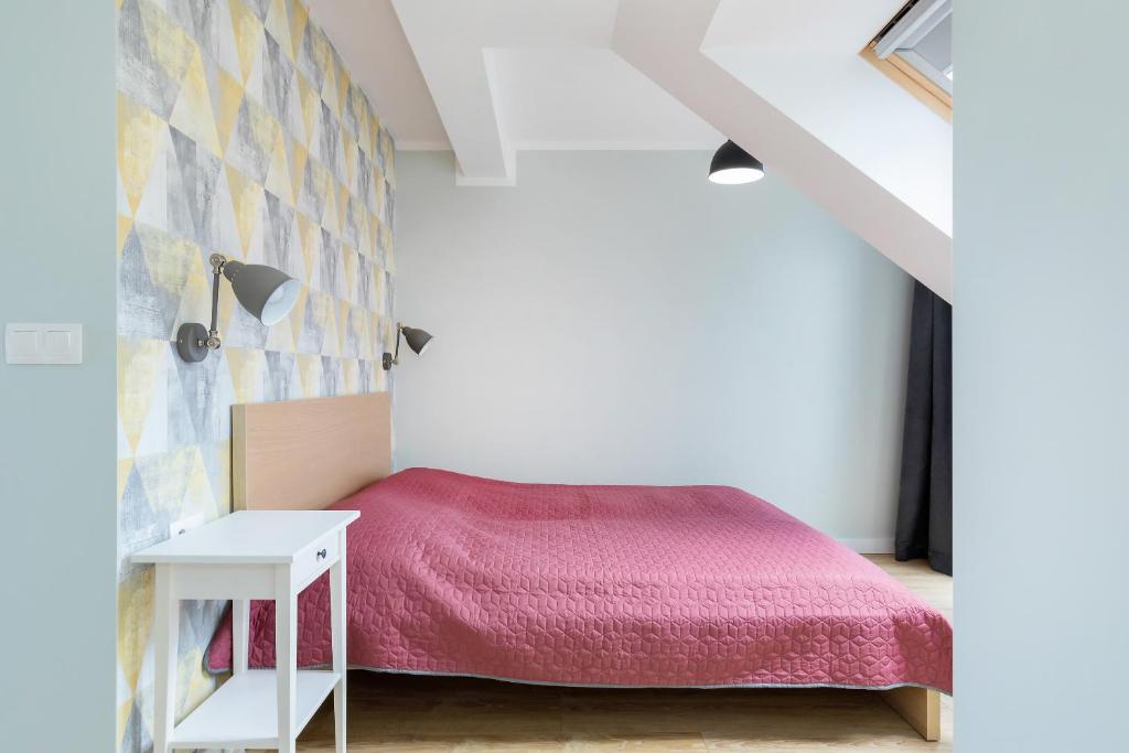 Wide shot of bed with patterned accent wall, bedside lamp and small white nightstand, hardwood floor.