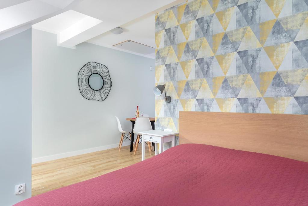 Angled bedroom view with red bed, decorative wall mirror, small dining table and chairs in background.