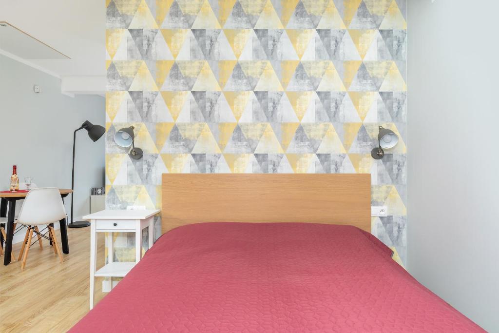 Center-framed wooden headboard with red bedspread against triangular patterned wallpaper, bedside table visible.