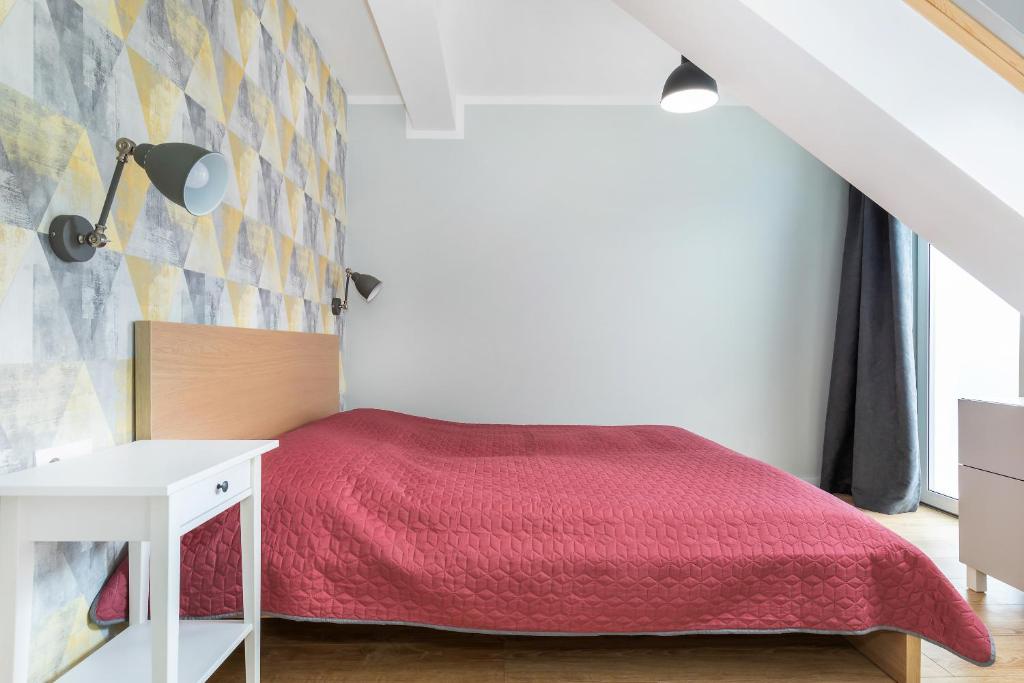 Cozy bedroom featuring red quilted bedspread, geometric yellow-gray accent wall, bedside lamp and table.