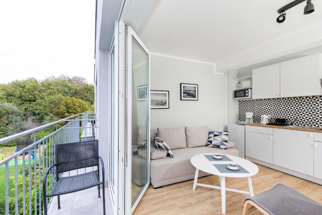 Open balcony door revealing chair, small outdoor seating, beige sofa and compact kitchenette inside.