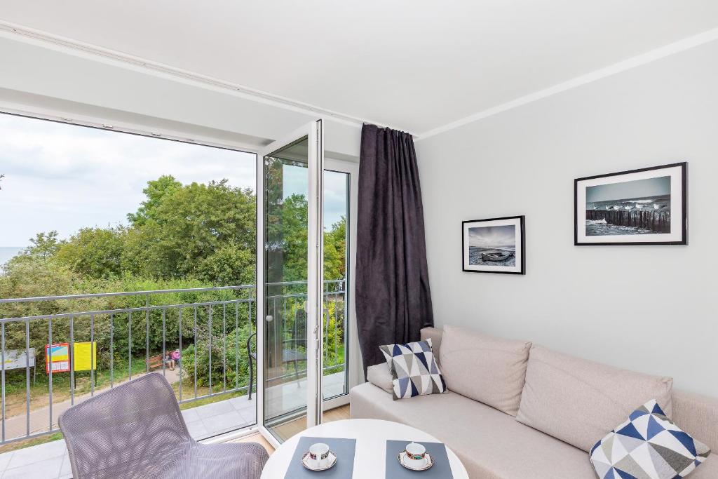 Sofa beside open glass door leading to balcony overlooking treed pathway and distant water