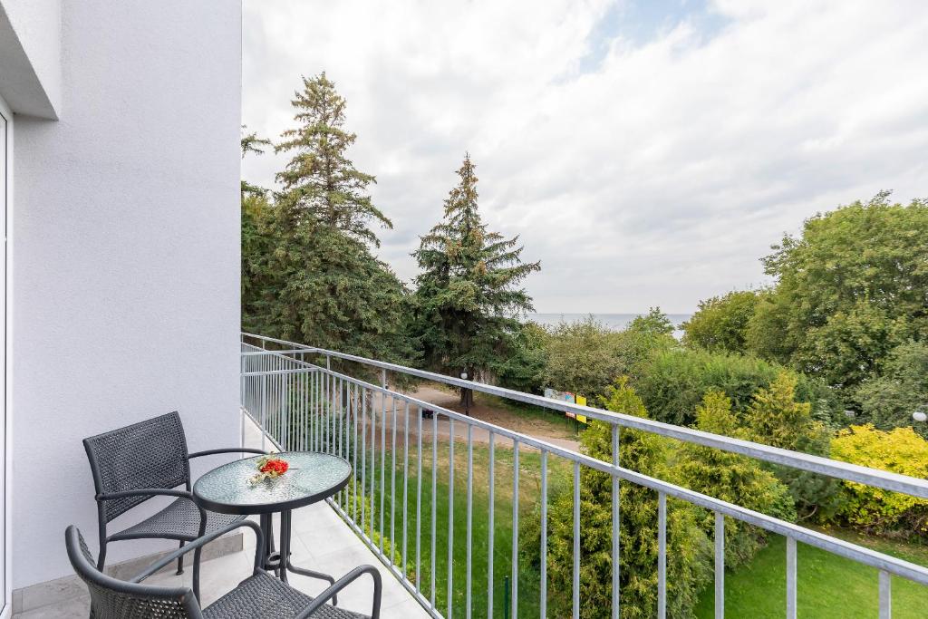 Narrow balcony with two black chairs and table, railing framing treetop sea view