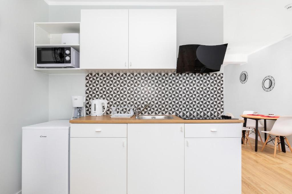 Minimal kitchenette with white cabinets, compact fridge, geometric backsplash and wooden countertop