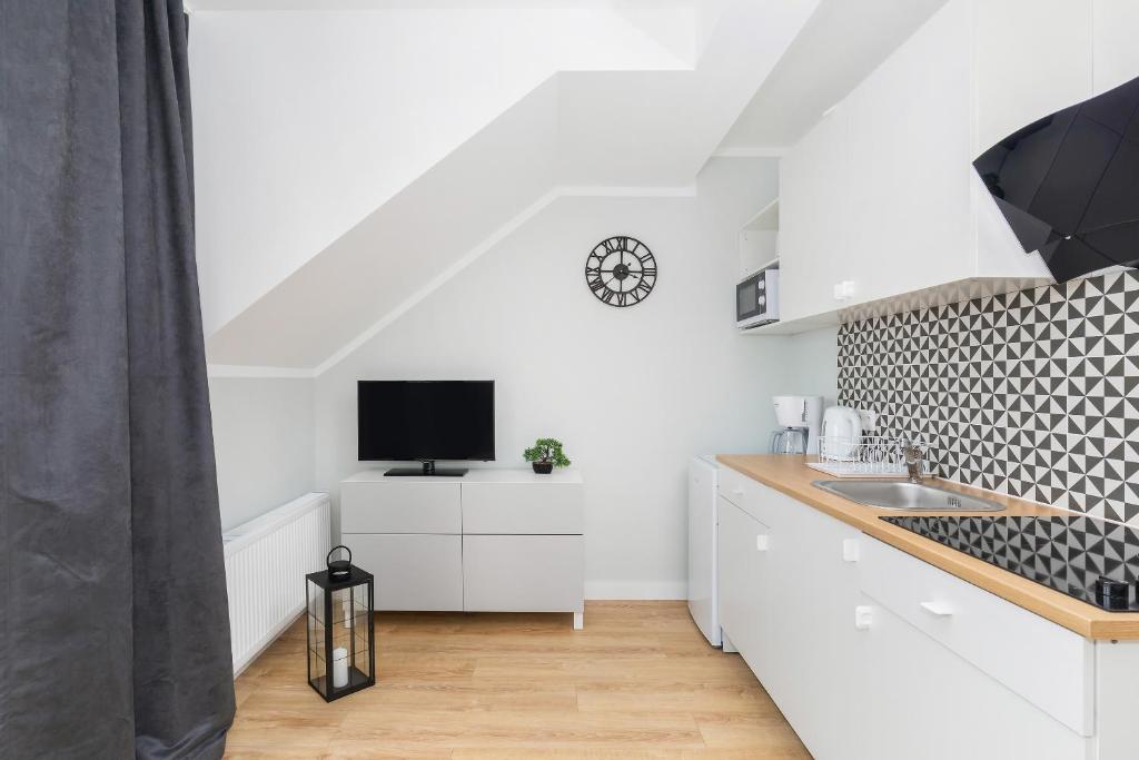 Compact studio interior showing TV on white dresser, patterned kitchenette, and wall clock